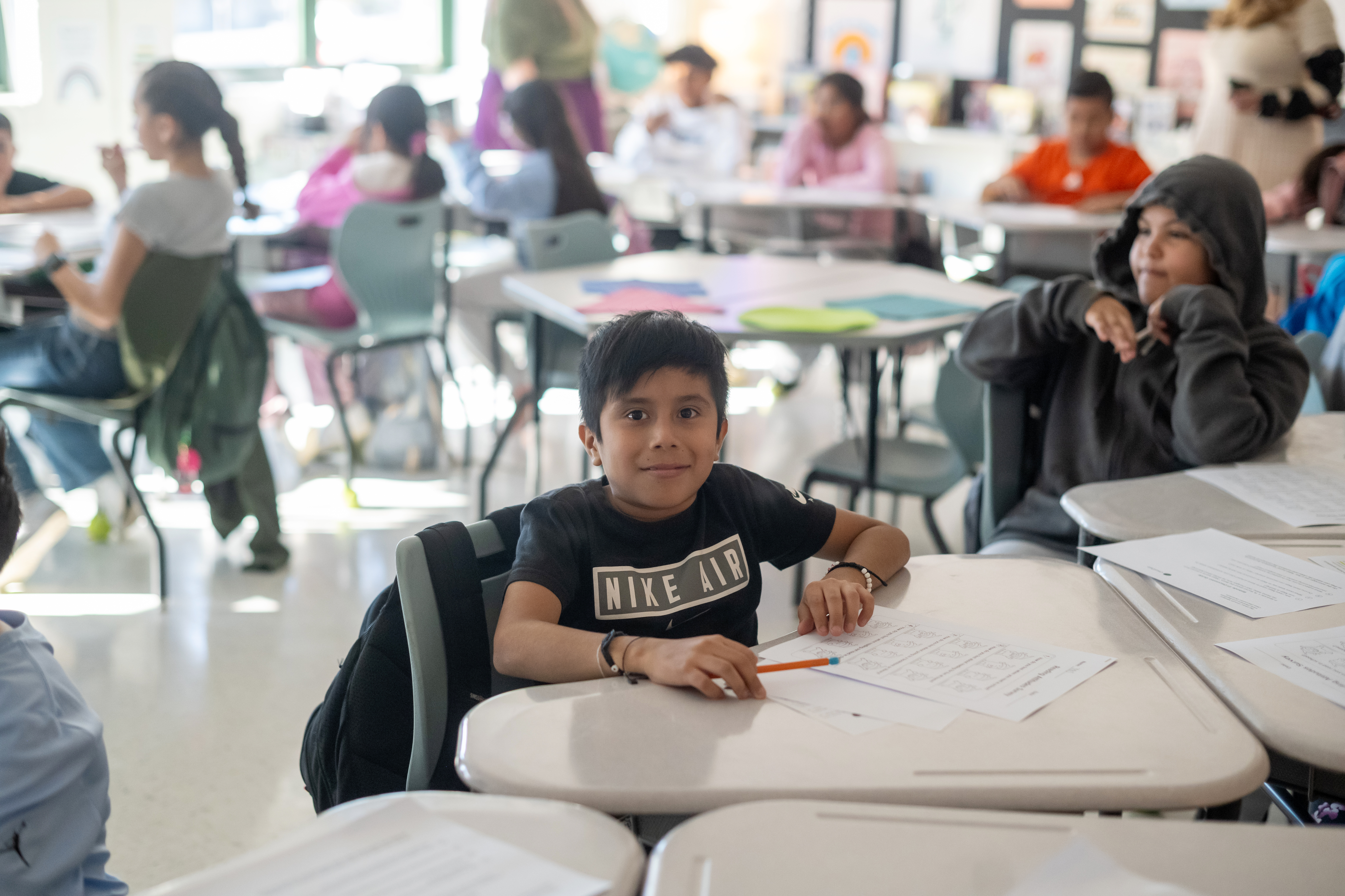 5th grade boy sitting at a gray desk in his classroom. 